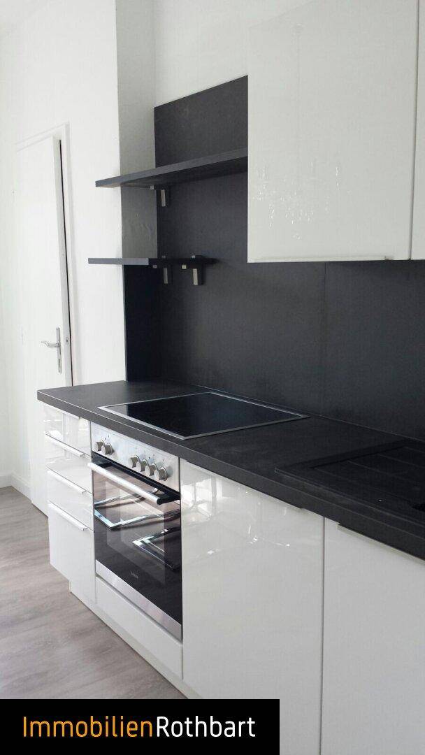 Detailansicht der modernen Küche mit integriertem Backofen und Induktionskochfeld. Weiße Schränke und schwarze Arbeitsplatte.