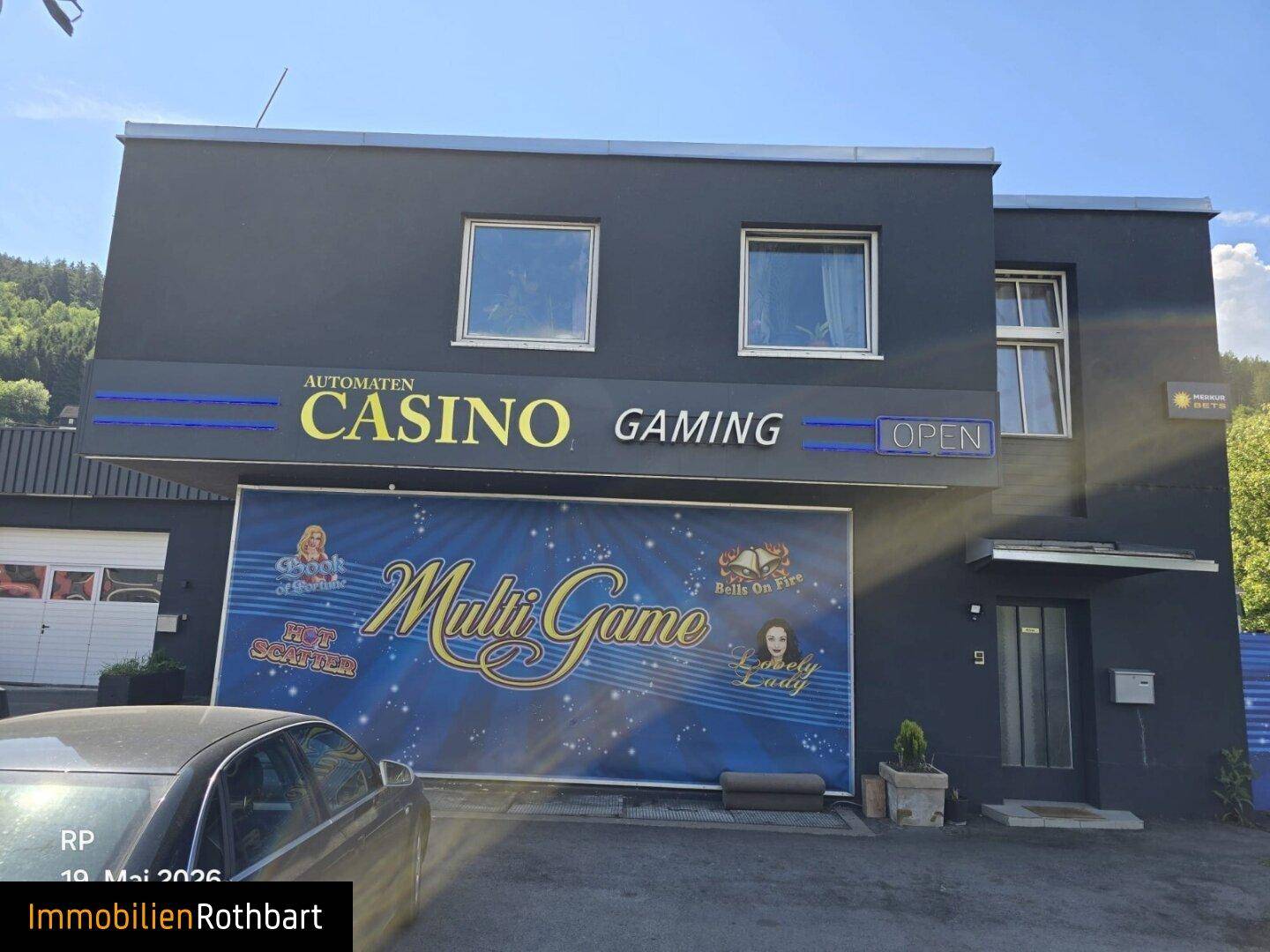 Vorderansicht des Geschäftsgebäudes mit Casino-Werbung und einem geparkten Auto im Vordergrund.