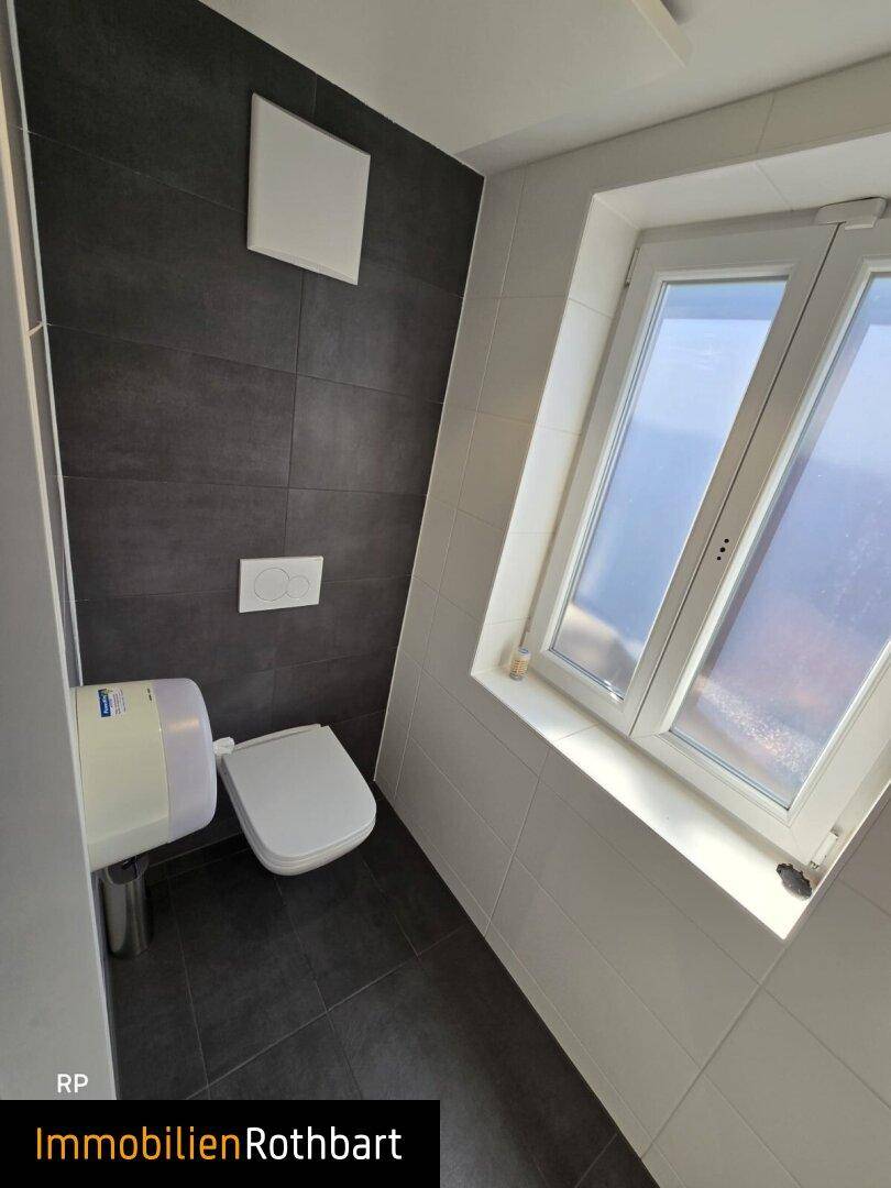 Moderne Toilette mit dunklen Fliesen, wandhängendem WC und einem Fenster für Tageslicht.