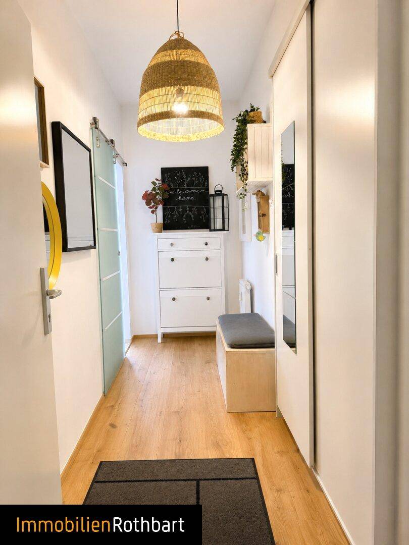 Heller Flur mit Holzfußboden, einer Sitzbank und einem Spiegelschrank, beleuchtet von einer Korblampe.