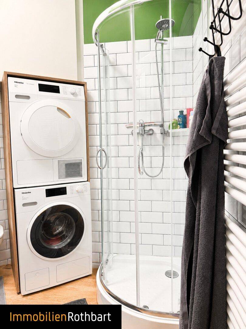 Modernes Badezimmer mit Duschkabine, Waschmaschine und Trockner, umgeben von weißen Fliesen.