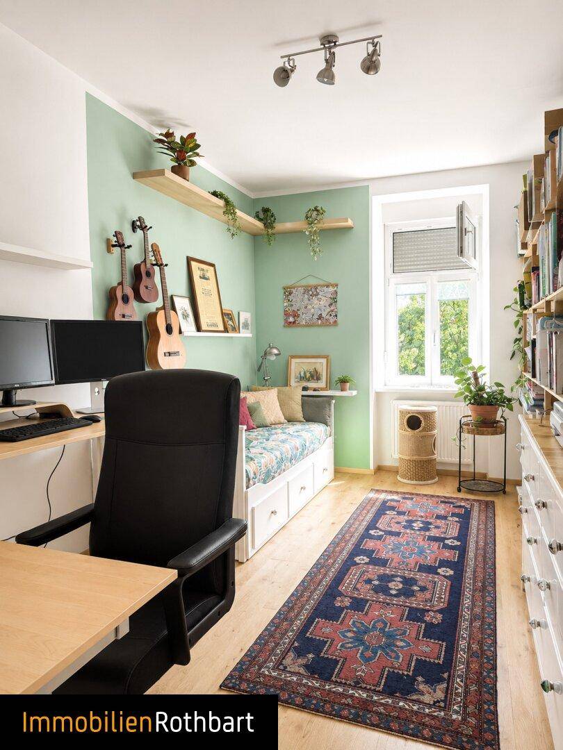 Arbeitszimmer mit Schreibtisch, Tagesbett und Bücherregal, hell gestrichen mit grüner Akzentwand.