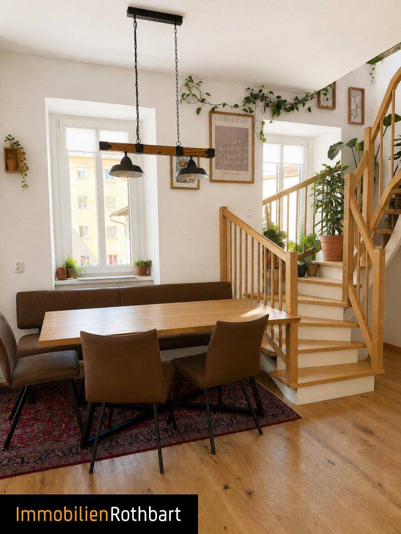 Heller Essbereich mit Holztisch, Sitzbank und einer Holztreppe, umgeben von Pflanzen.