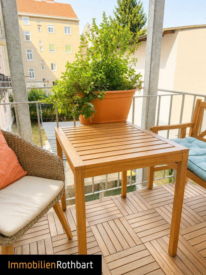 Heller Balkon mit Holzbodenfliesen und einem Holztisch, ideal für Mahlzeiten im Freien.