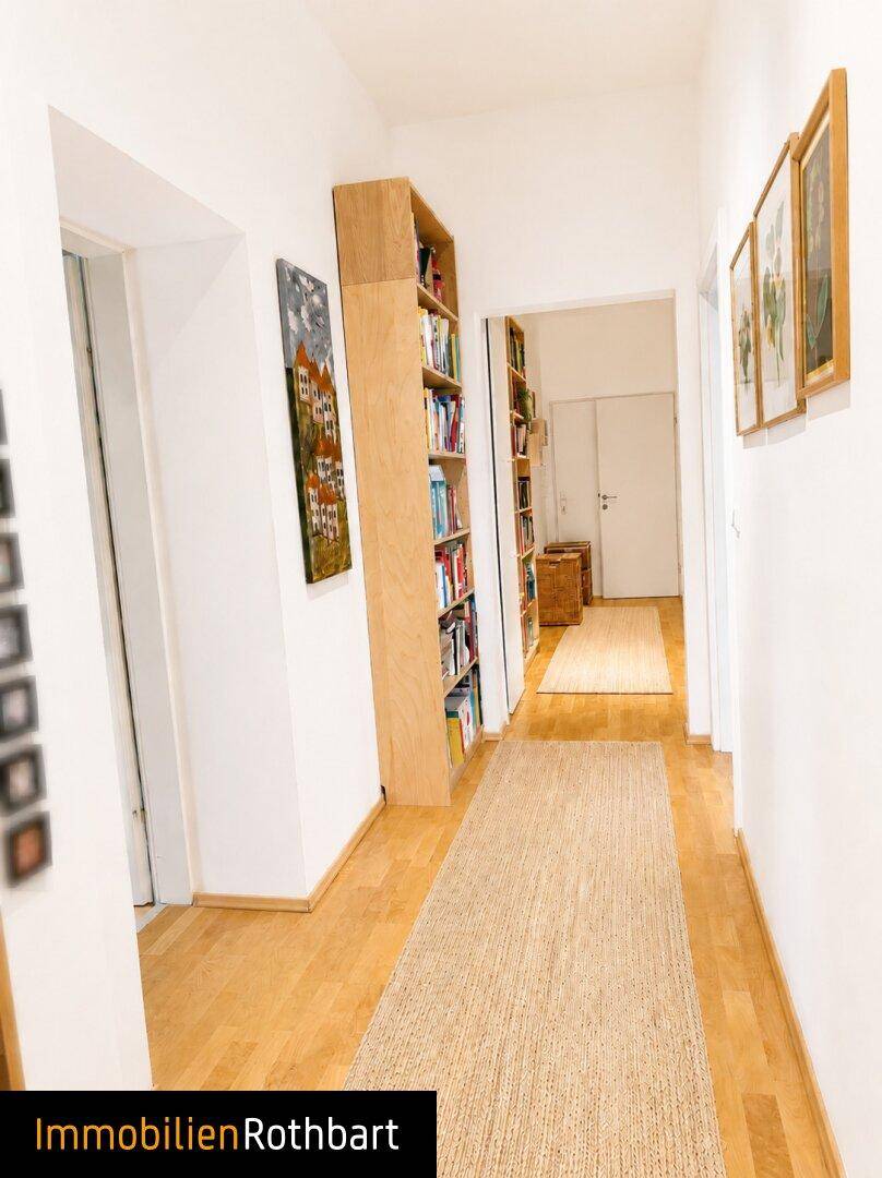 Langer Flur mit Holzfußboden und Bücherregalen, der zu weiteren Räumen führt.