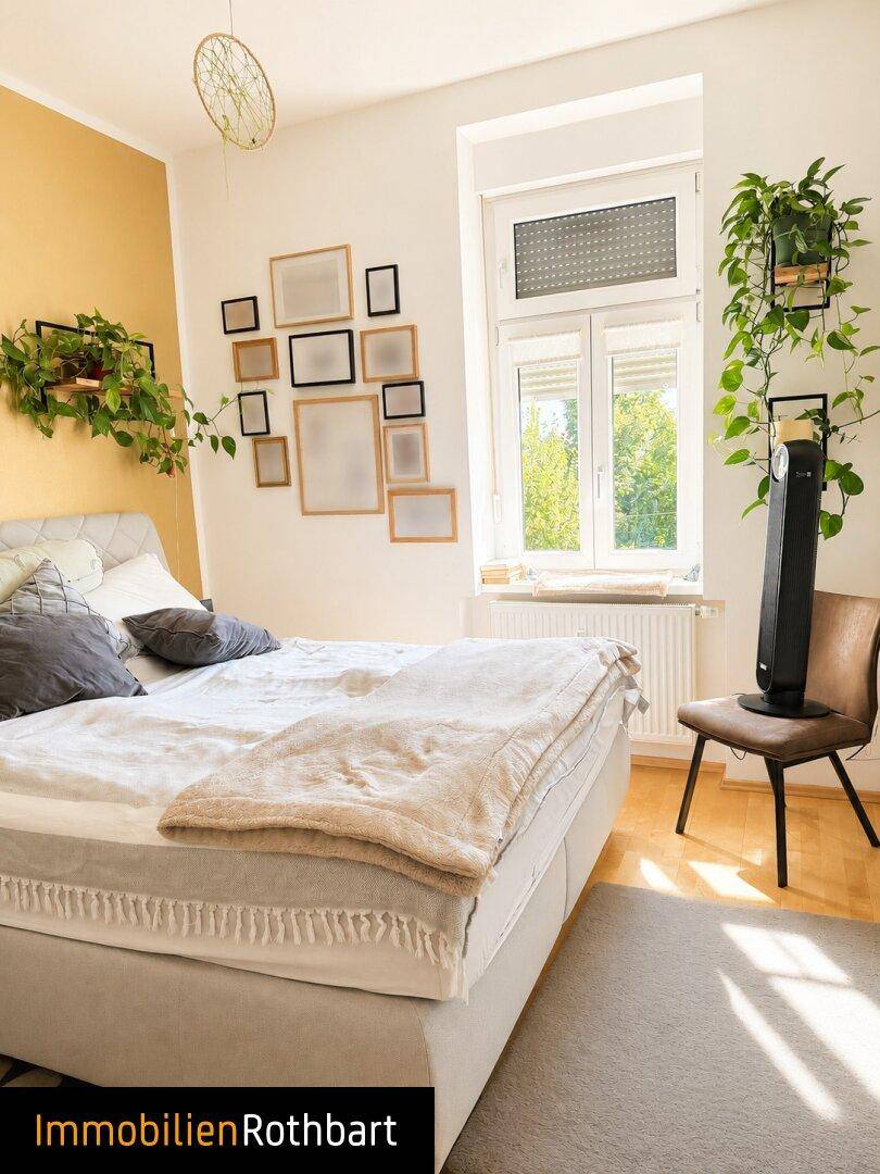 Helles Schlafzimmer mit Doppelbett, Holzboden und einem Fenster mit Blick ins Grüne.