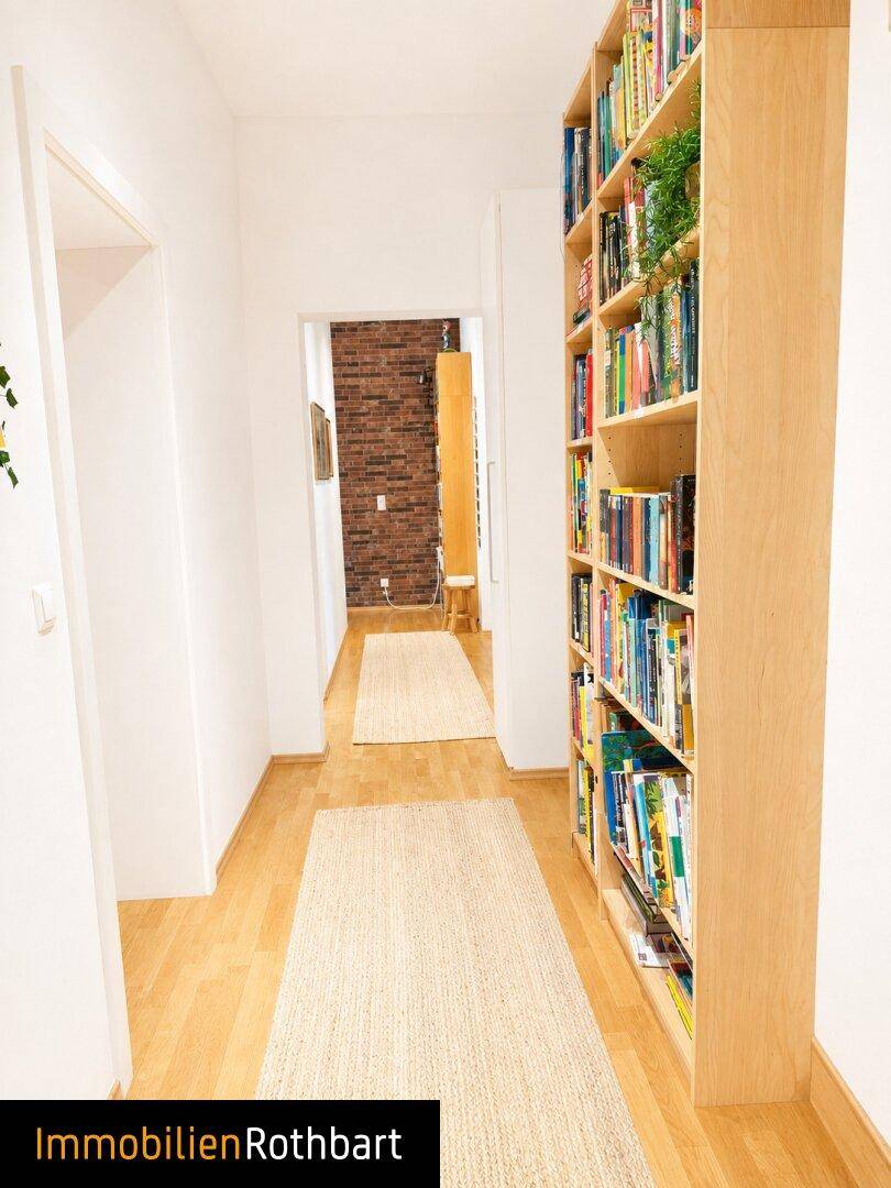 Heller Flur mit Holzfußboden und einem hohen Bücherregal, das viel Stauraum bietet.