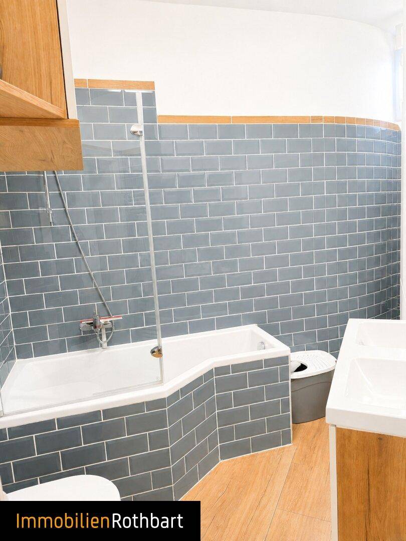 Badezimmer mit blauen U-Bahn-Fliesen, Badewanne mit Duschabtrennung und Holzfußboden.