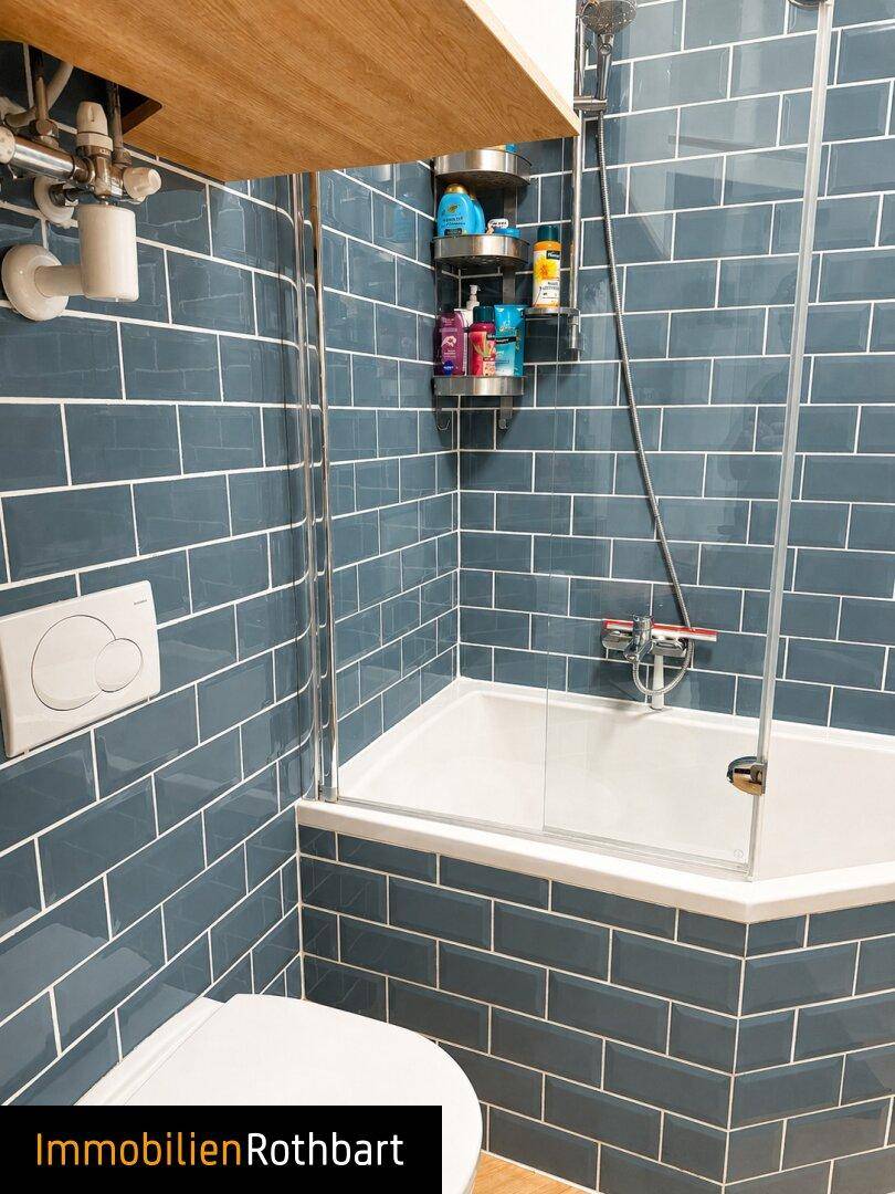 Badezimmer mit blauen U-Bahn-Fliesen, Badewanne mit Duschabtrennung und Wand-WC.