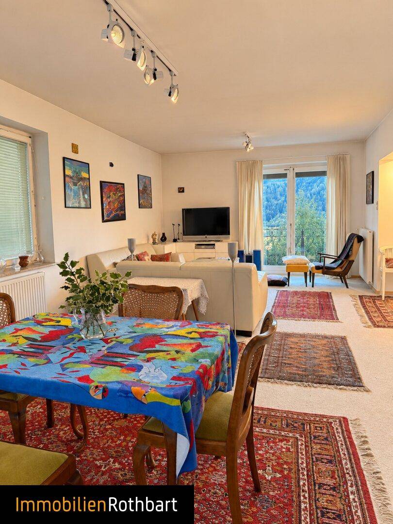 Heller Wohn- und Essbereich mit Sofa, Esstisch und Blick ins Grüne durch große Fenster.