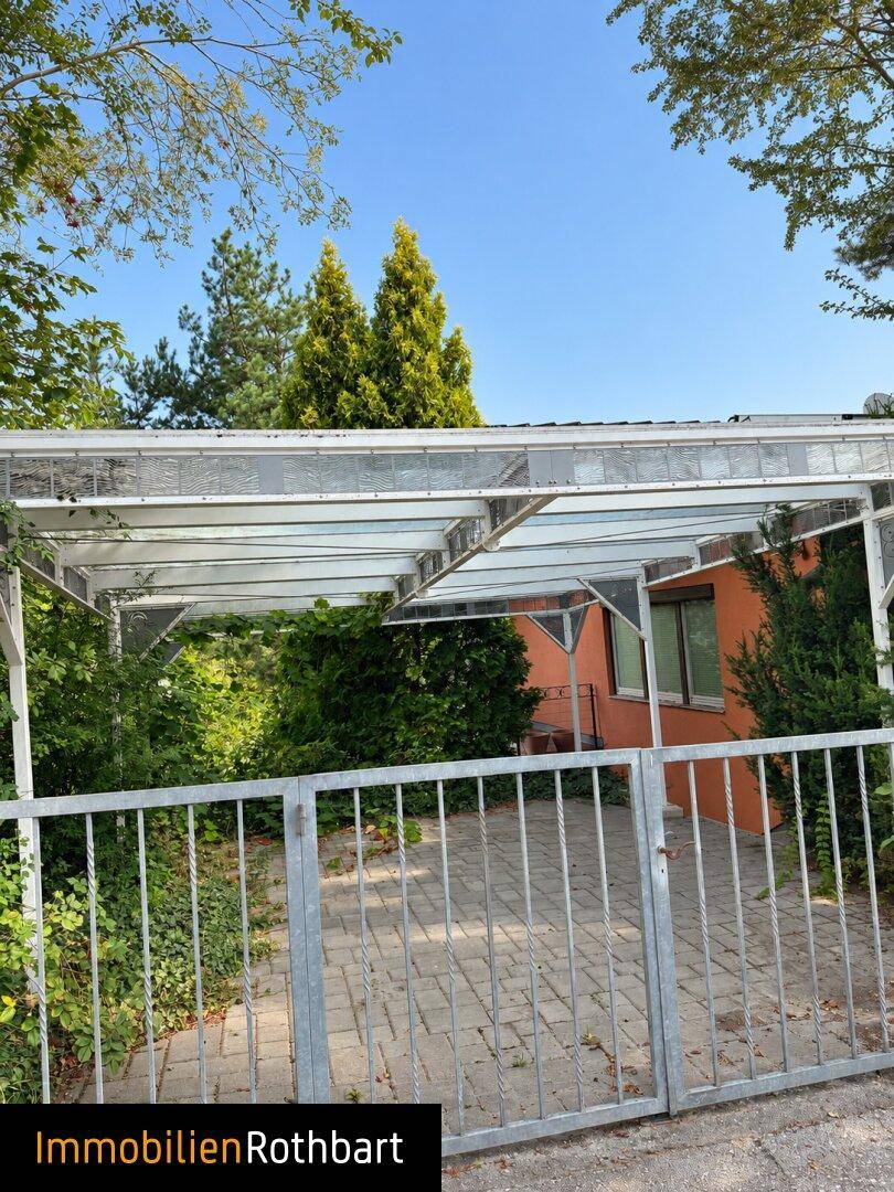 Überdachter Stellplatz oder Carport mit gepflastertem Bereich und umgebendem Grün.