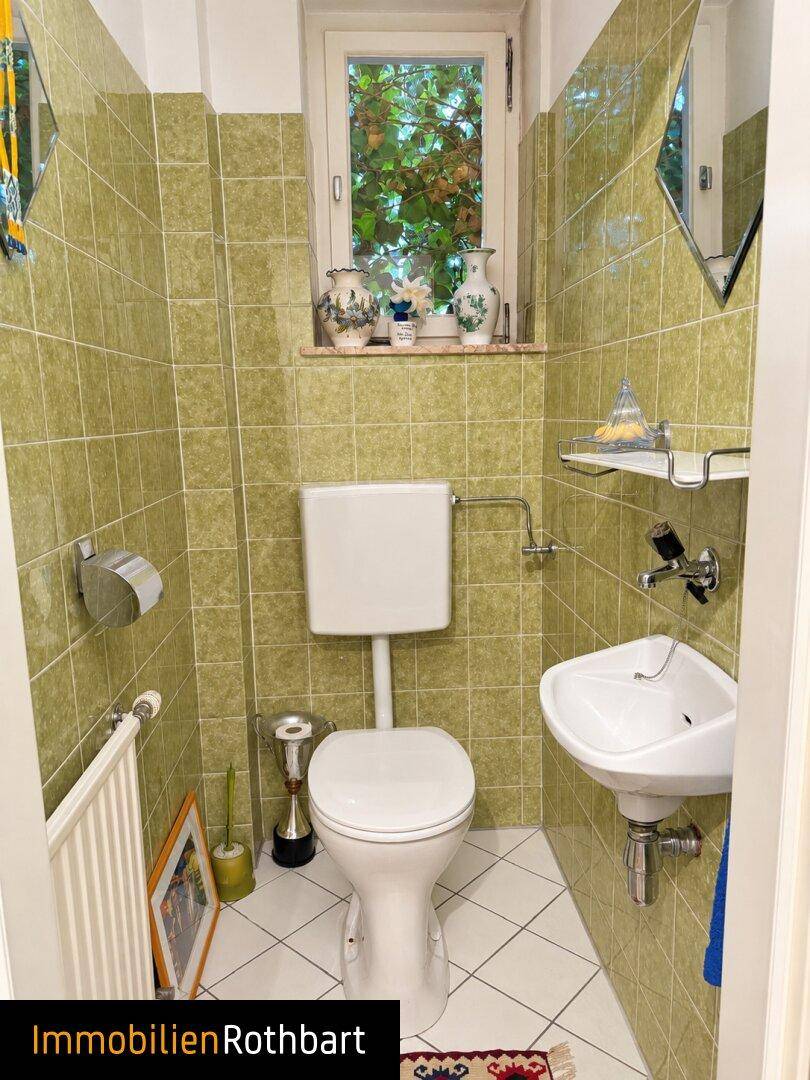 Gäste-WC mit grünen Fliesen, Fenster und kleinem Waschbecken.