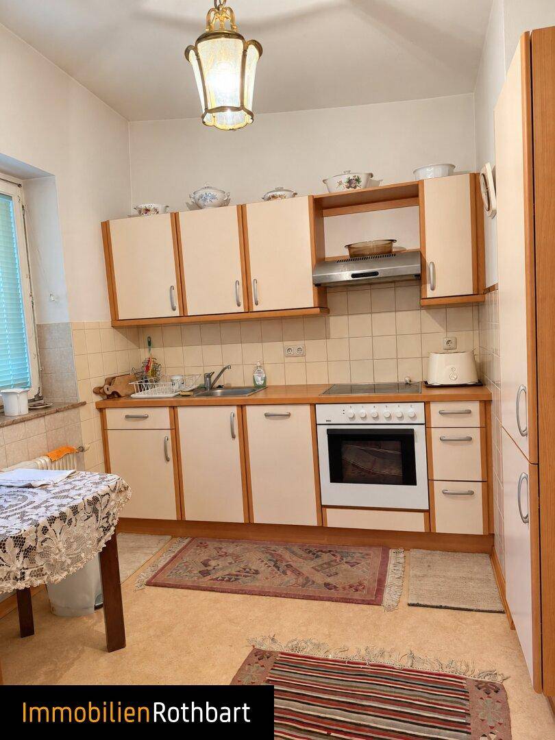 Funktionale Küche mit hellen Holzfronten, Einbaugeräten und kleinem Essbereich am Fenster.
