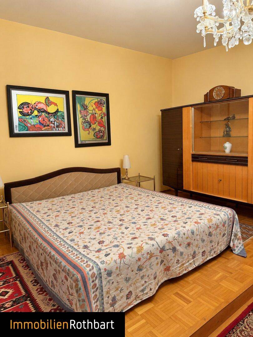 Geräumiges Schlafzimmer mit Doppelbett, Holzschrank und Kronleuchter, in warmen Farbtönen gehalten.