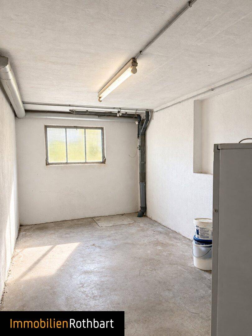 Einfacher Abstellraum mit Fenster, Betonboden und sichtbaren Rohren im Kellerbereich.