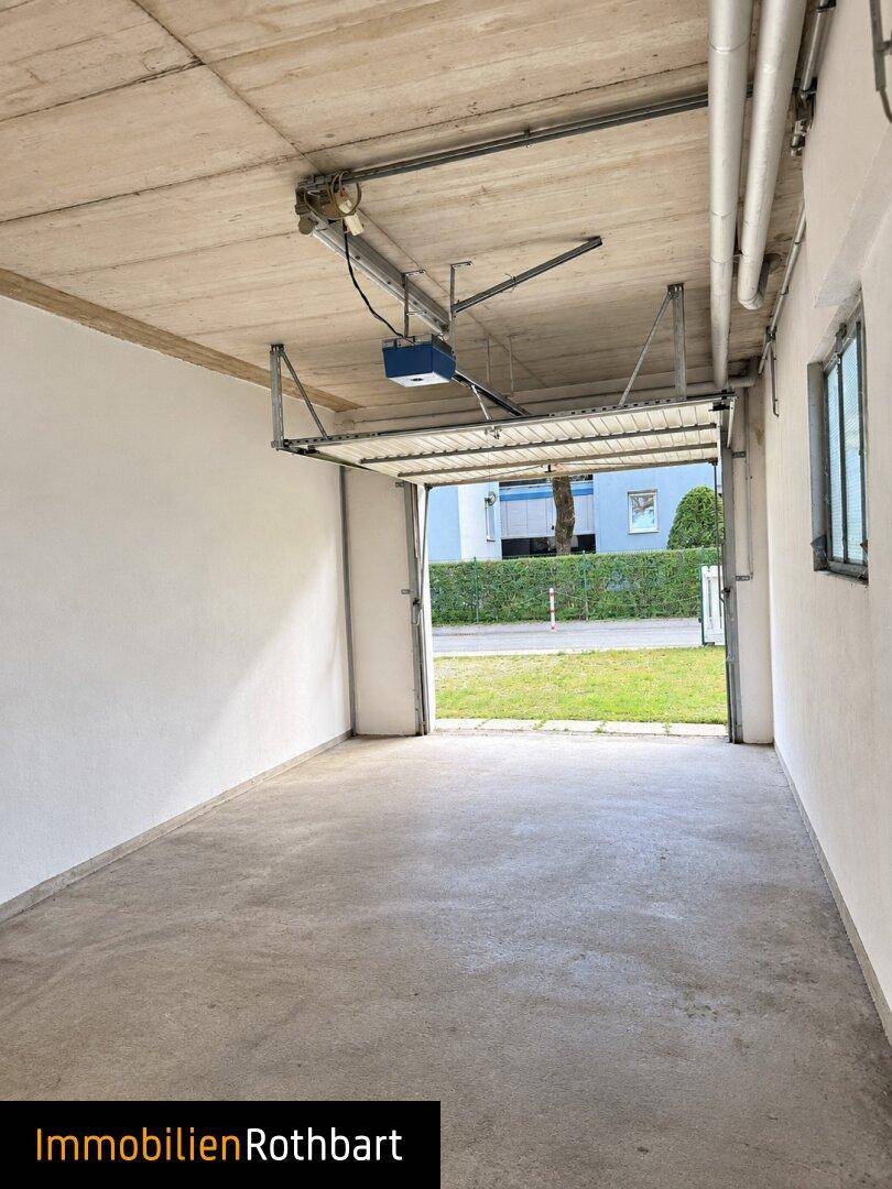 Geräumige Garage mit automatischem Tor und Fenster zur Straße, ideal für ein Fahrzeug.
