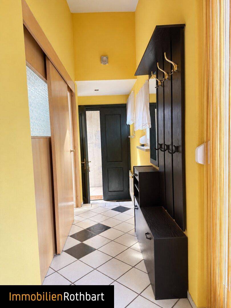 Eingangsbereich mit gelben Wänden, Fliesenboden und Garderobe.