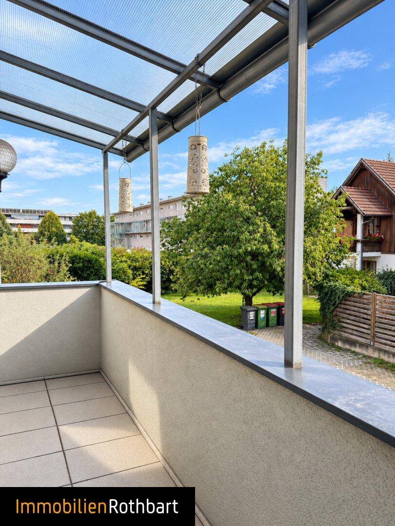 Überdachter Balkon mit Fliesenboden und Blick auf die Umgebung und Industriegebäude.