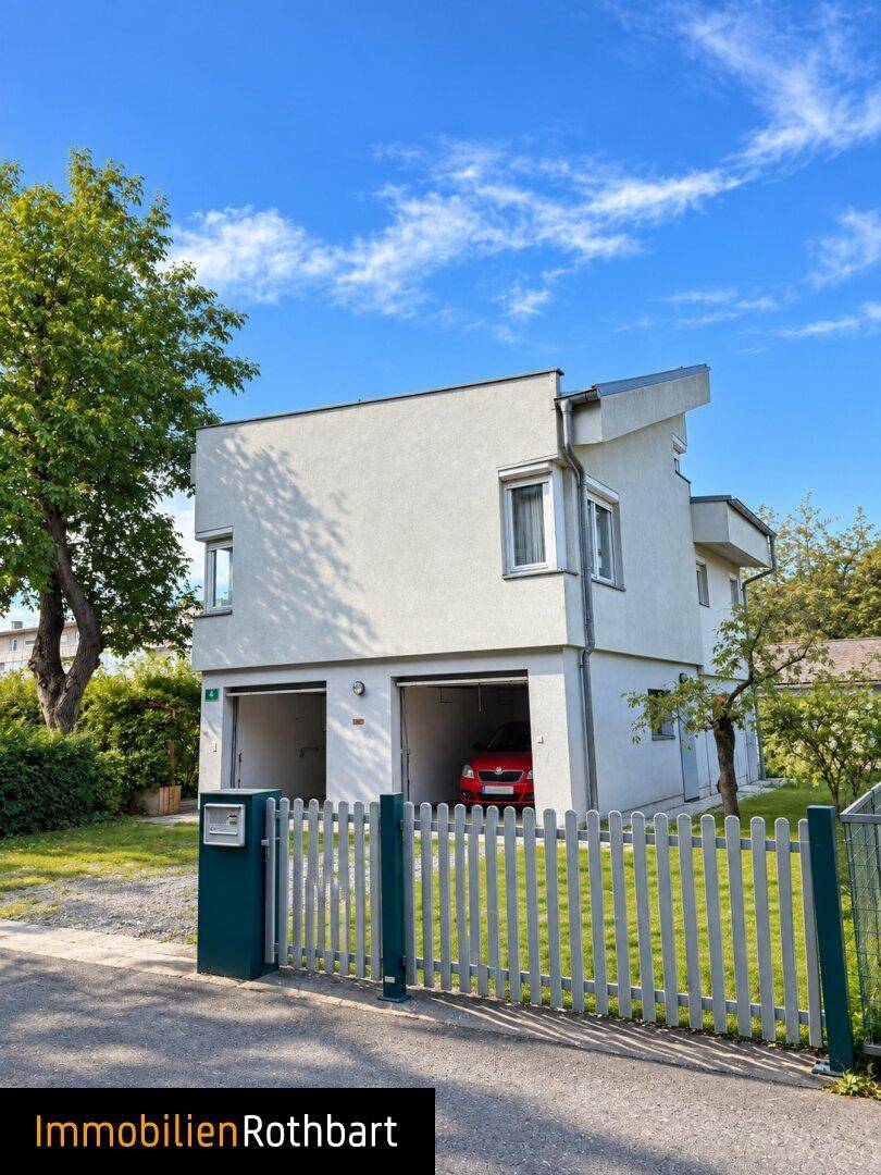 Ansicht des modernen Hauses mit integrierten Garagen und gepflegtem Vorgarten unter blauem Himmel.