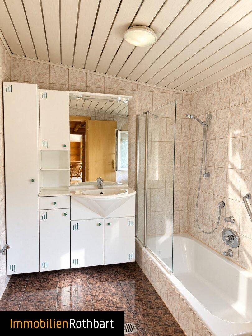 Badezimmer mit Badewanne, Dusche, Einzelwaschbecken und gefliesten Wänden.