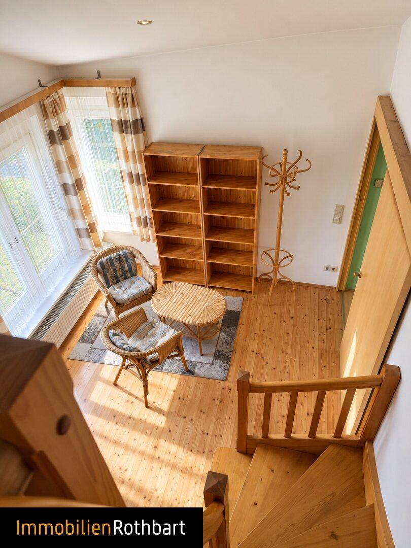 Gemütlicher Wohnbereich mit Holzfußboden, Korbmöbeln und großen Fenstern.