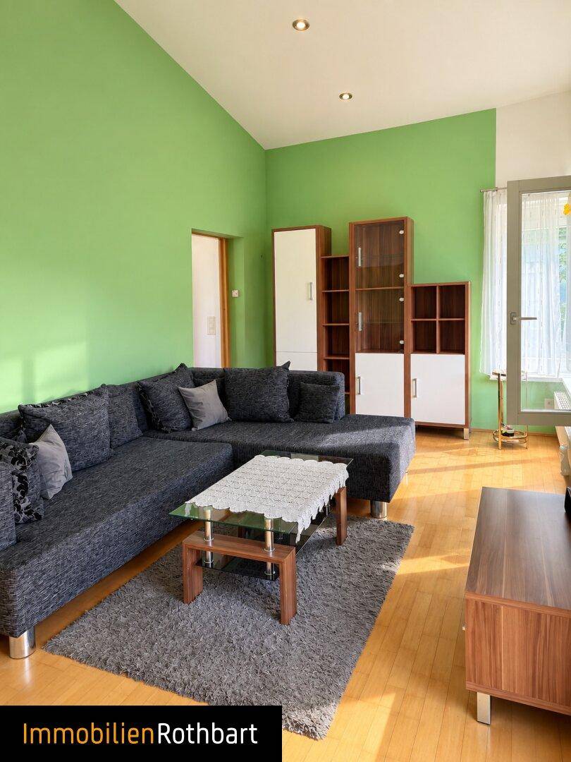 Helles Wohnzimmer mit grünen Wänden, großem Sofa und Holzfußboden.