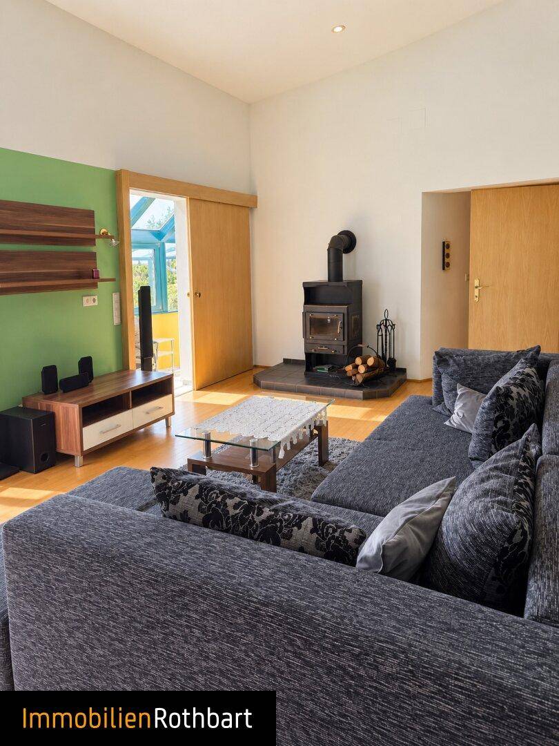 Gemütliches Wohnzimmer mit Kaminofen, großem Sofa und Zugang zum Wintergarten.
