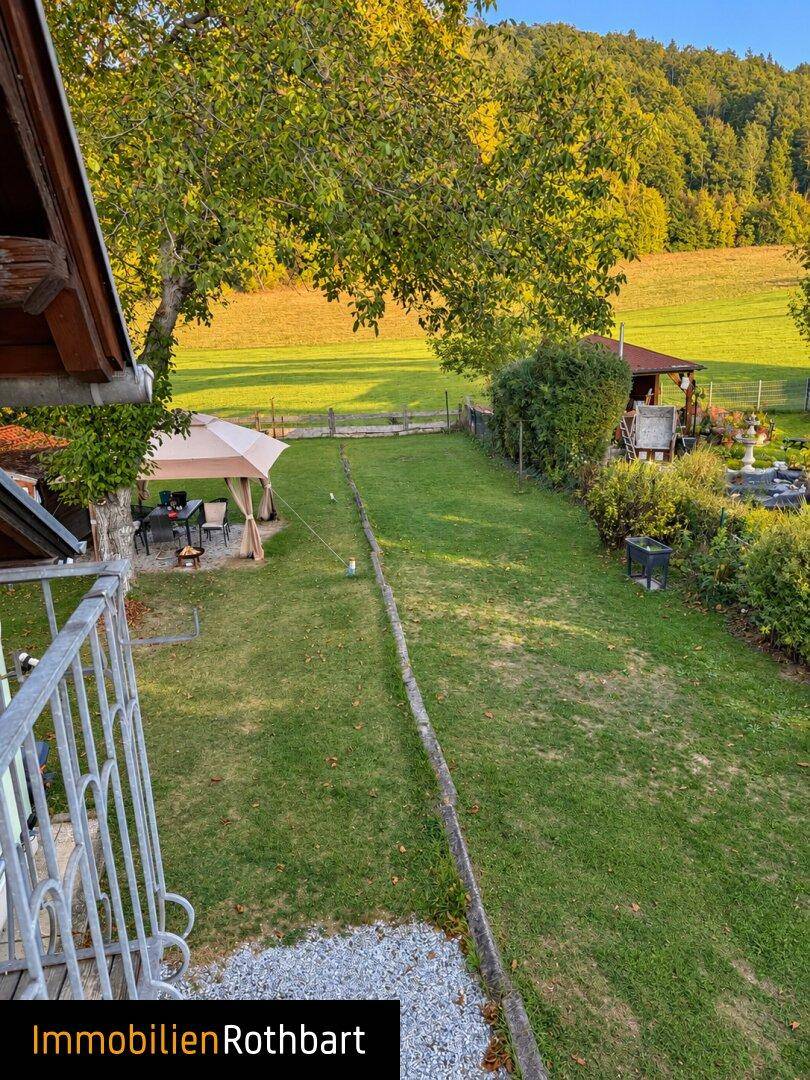 Weitläufiger Blick vom Balkon auf den Garten mit Rasenfläche, Bäumen und einem Pavillon.
