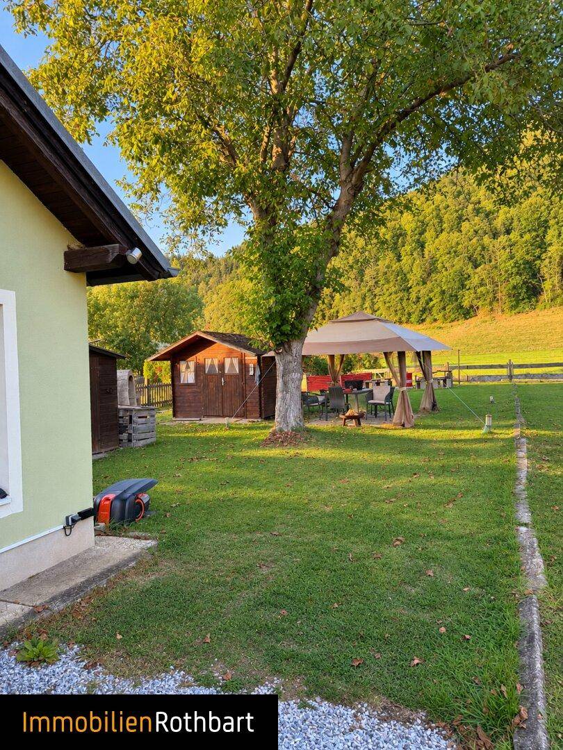 Großer, gepflegter Garten mit Rasenfläche, schattenspendendem Baum und einem Pavillon mit Sitzgelegenheiten.
