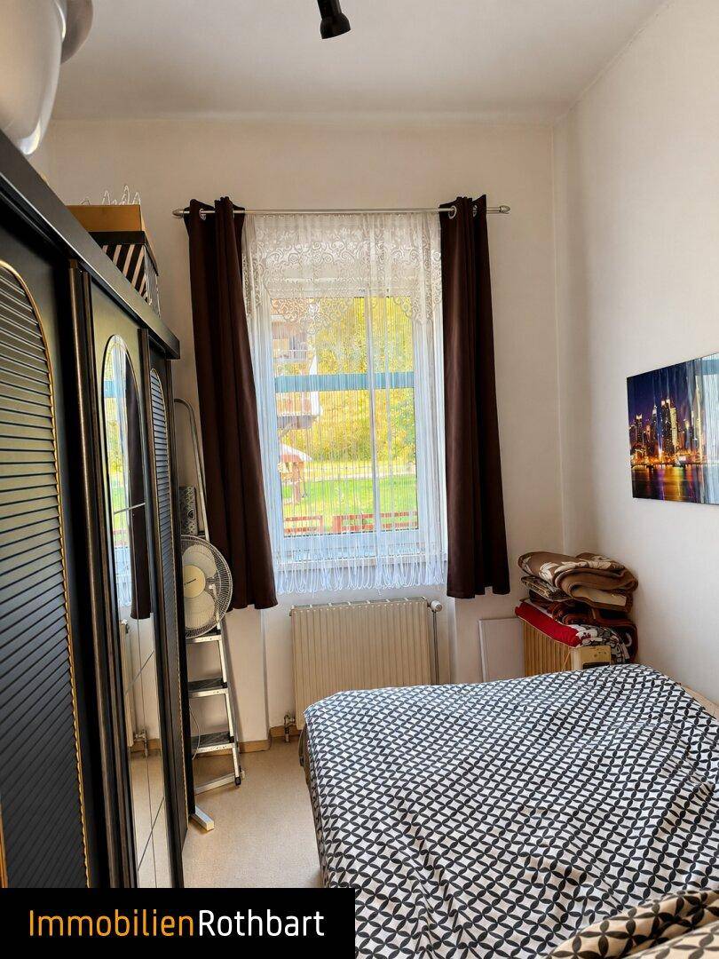 Schlafzimmer mit Teppichboden, Doppelbett und einem großen Kleiderschrank, hell durch das Fenster.