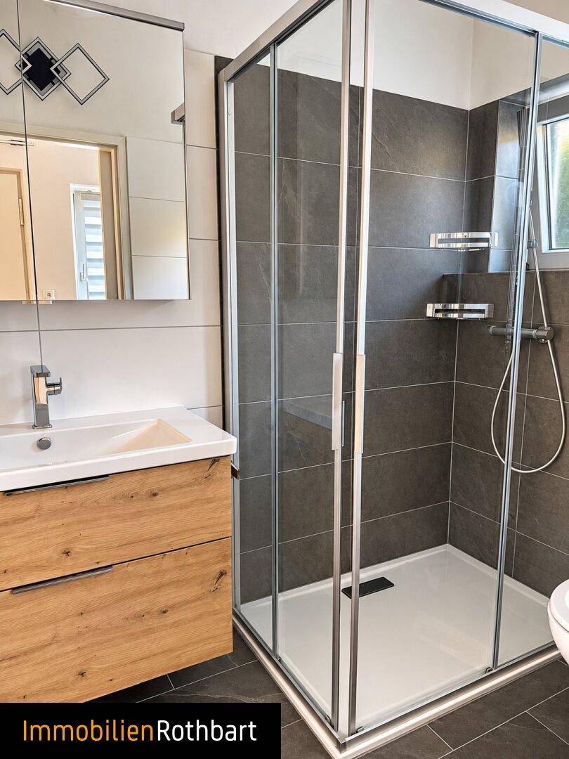 Modernes Badezimmer mit dunklen Fliesen, Holzwaschtisch und einer geräumigen Duschkabine.