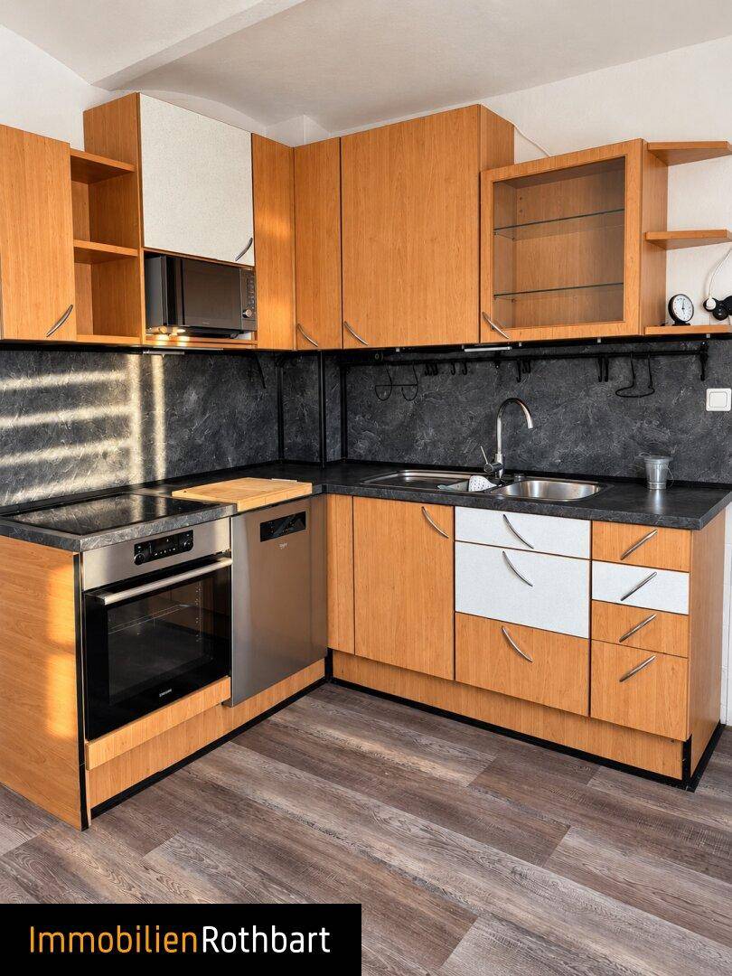Moderne Einbauküche mit Holzfronten, dunkler Arbeitsplatte und integriertem Geschirrspüler.