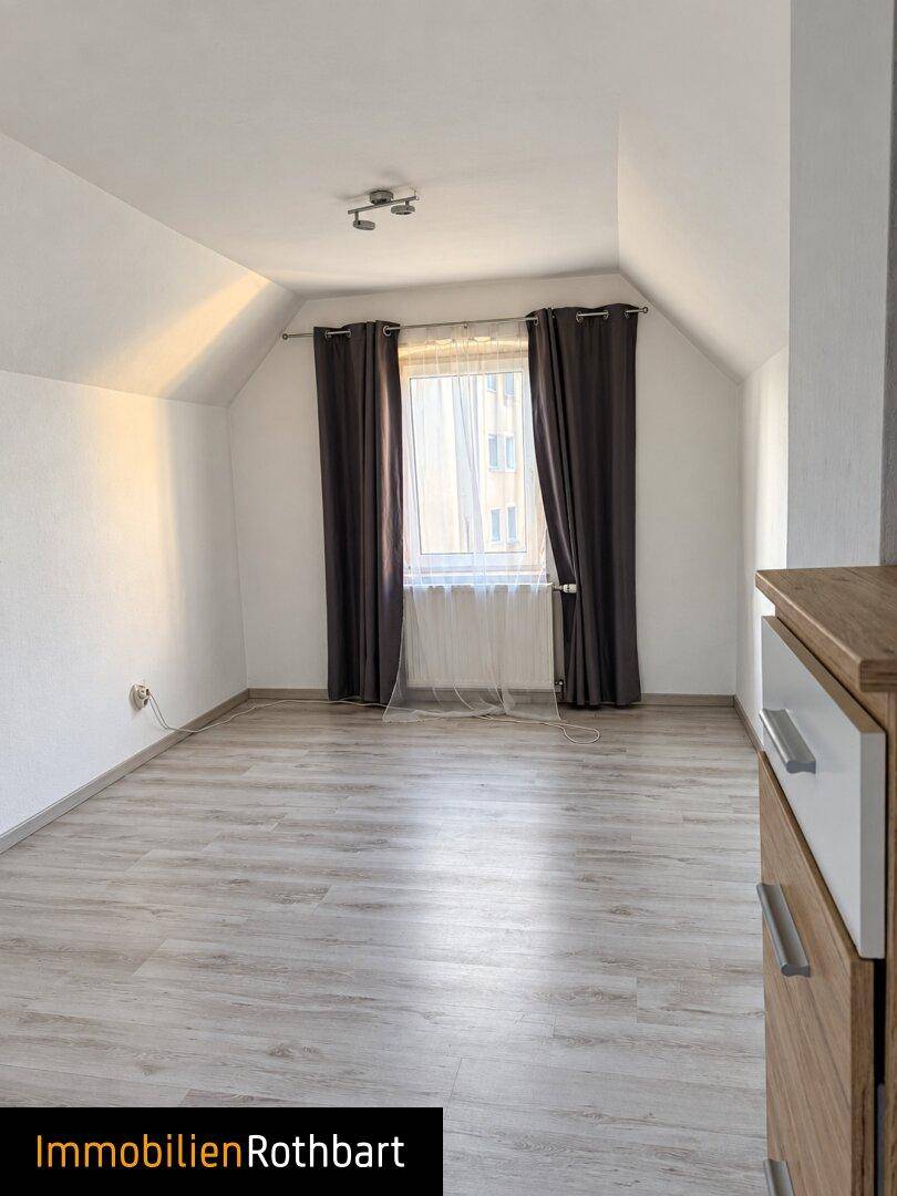 Helles Schlafzimmer im Dachgeschoss mit Laminatboden und einem Fenster, das viel Licht hereinlässt.
