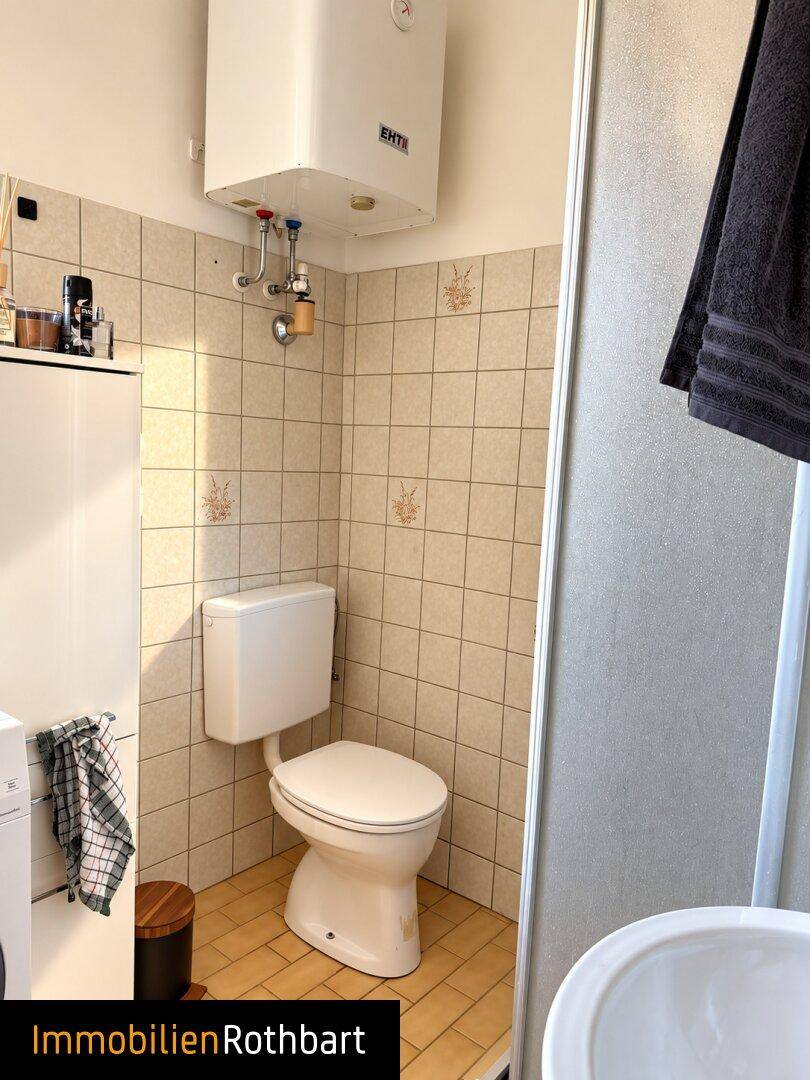 Kleines Badezimmer mit WC, Dusche und Fliesen im Retro-Stil, inklusive Warmwasserboiler.