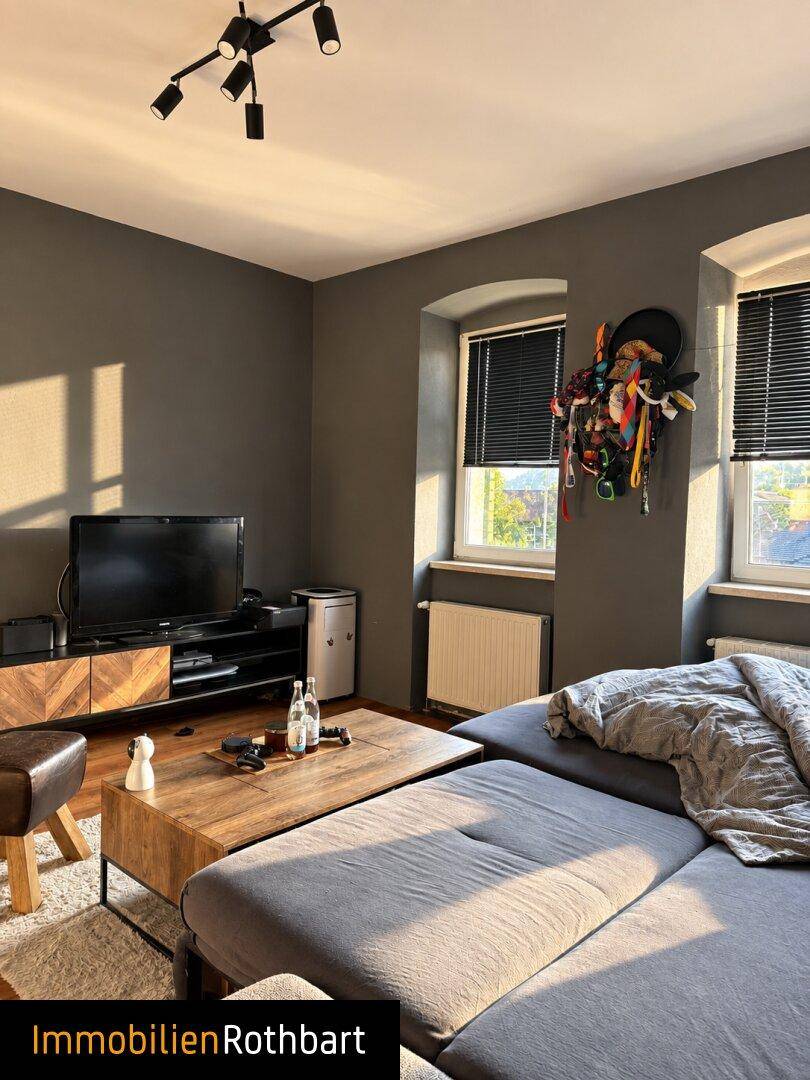 Gemütliches Wohnzimmer mit dunklen Wänden, großem Sofa und einem Fernseher auf einem Sideboard.