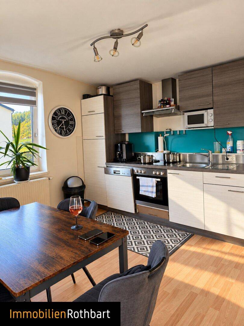 Moderne Küche mit Essbereich, Holztisch und zweifarbigen Schränken, gut beleuchtet.