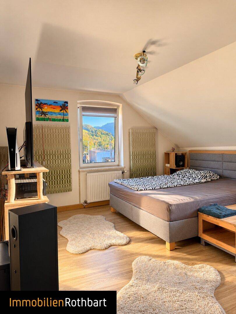 Schlafzimmer im Dachgeschoss mit Doppelbett, Holzboden und Blick auf die umliegende Landschaft.