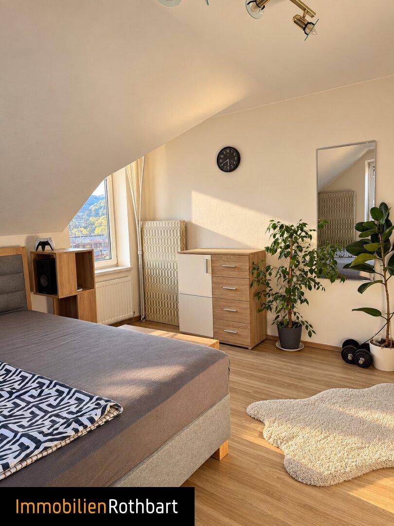 Helles Schlafzimmer im Dachgeschoss mit Holzboden, Pflanzen und einem Fenster mit Bergblick.