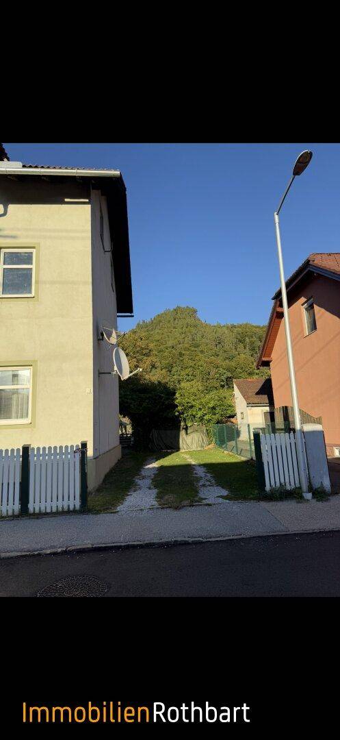 Seitenansicht eines Hauses mit Schotterauffahrt und Blick auf bewaldete Hügel im Hintergrund.