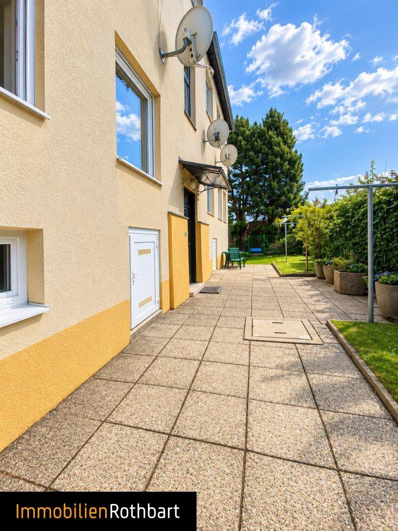 Gepflasterter Weg entlang des Hauses mit Rasenfläche und Hecke im Gartenbereich.