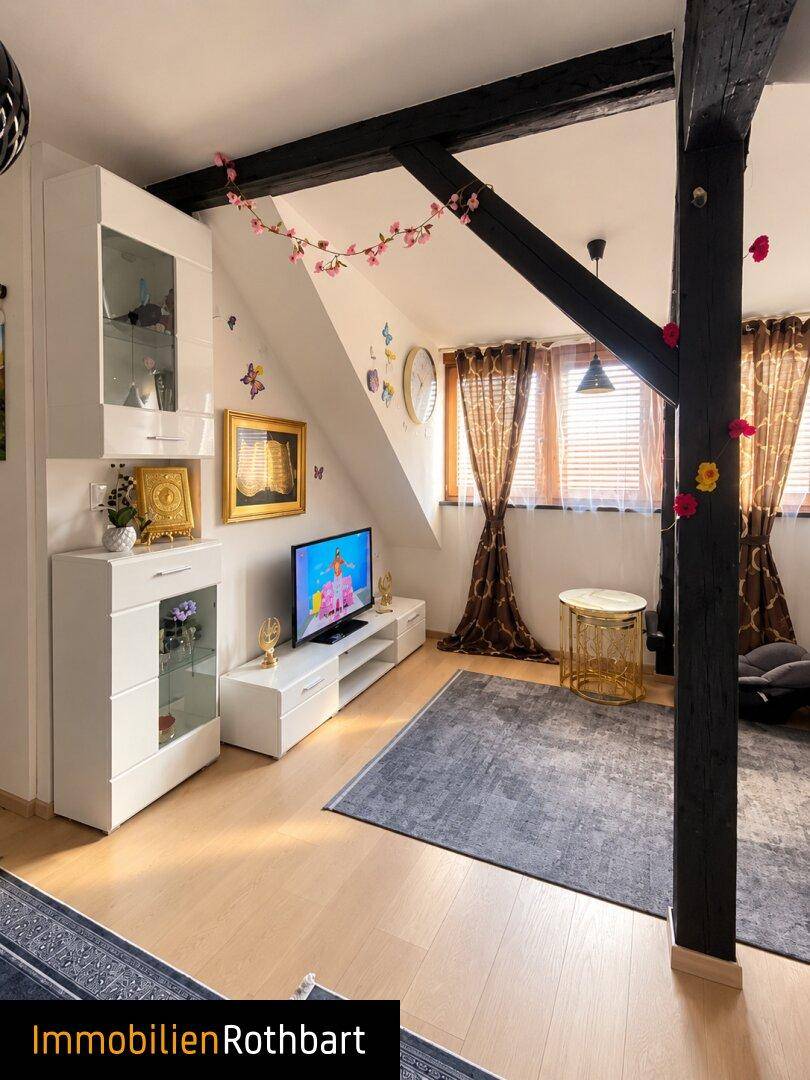 Wohnzimmer im Dachgeschoss mit Fernseher, Holzbalken und dekorativen Blumenranken.