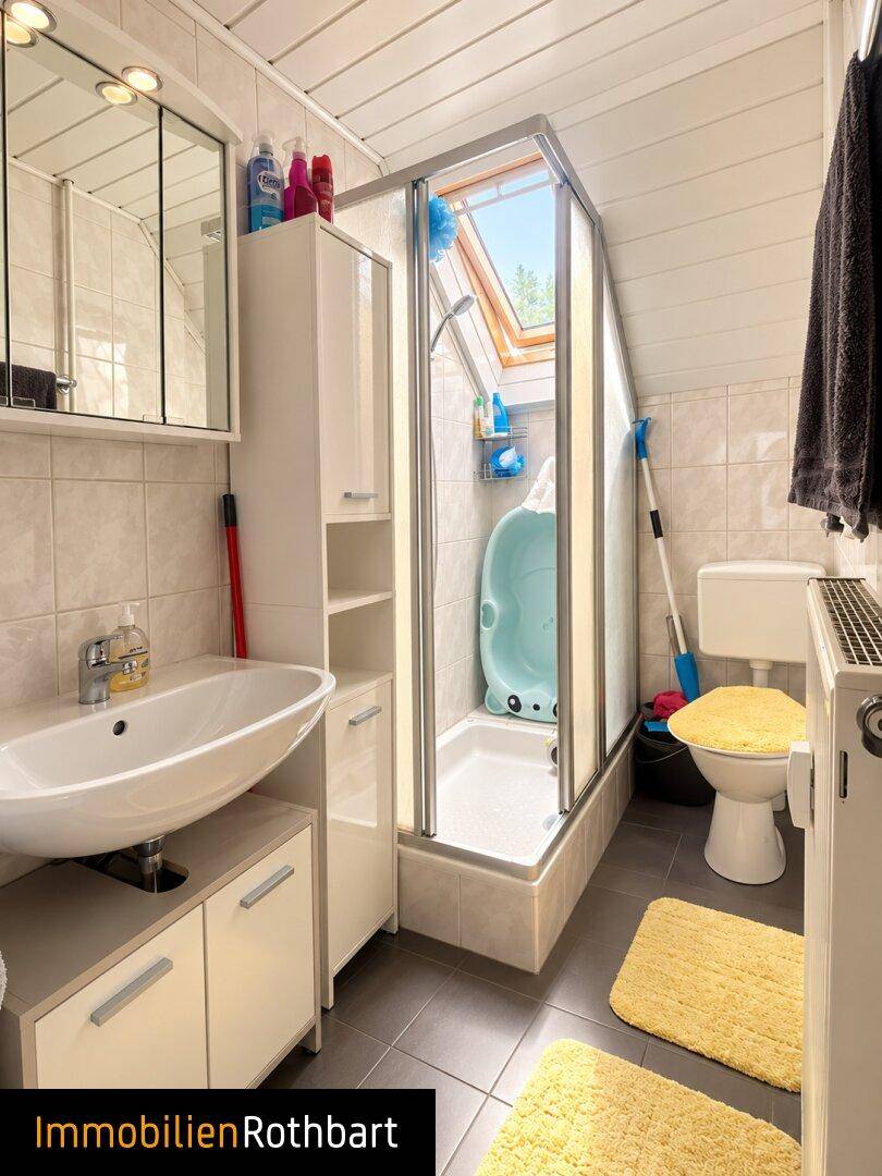 Kleines Badezimmer mit Dusche, Waschbecken, WC und Dachfenster für Tageslicht.