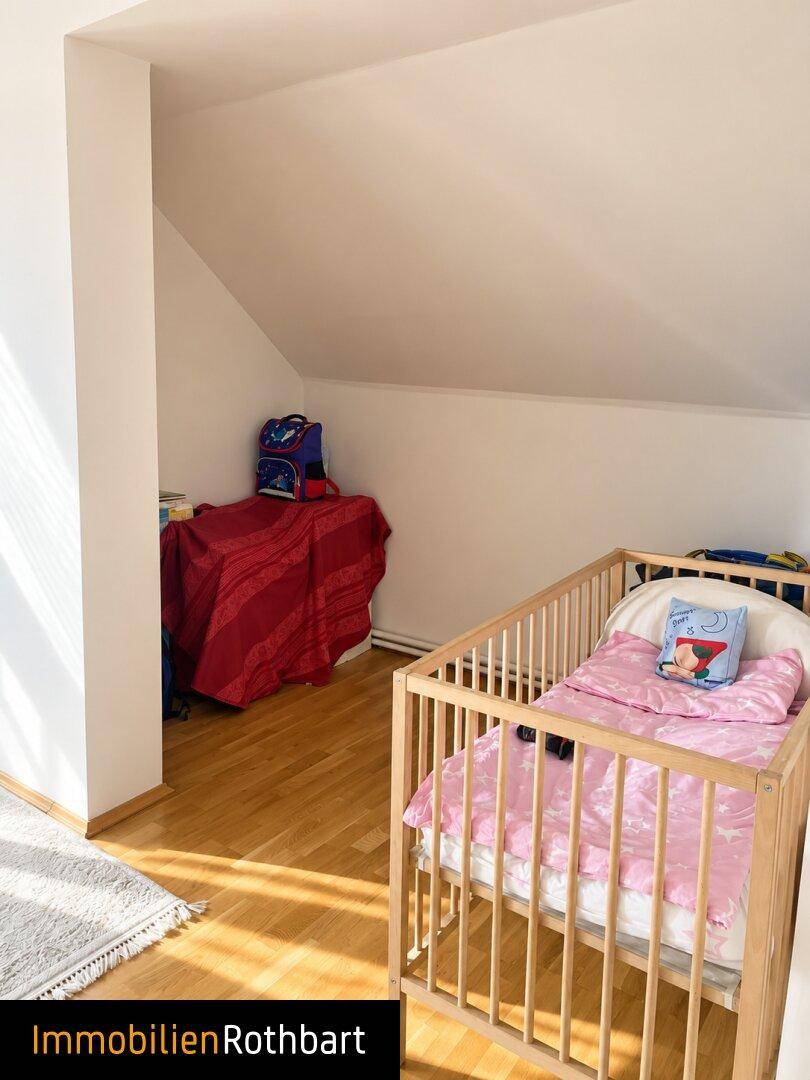 Kinderzimmer im Dachgeschoss mit Babybett, Holzboden und schrägen Wänden.
