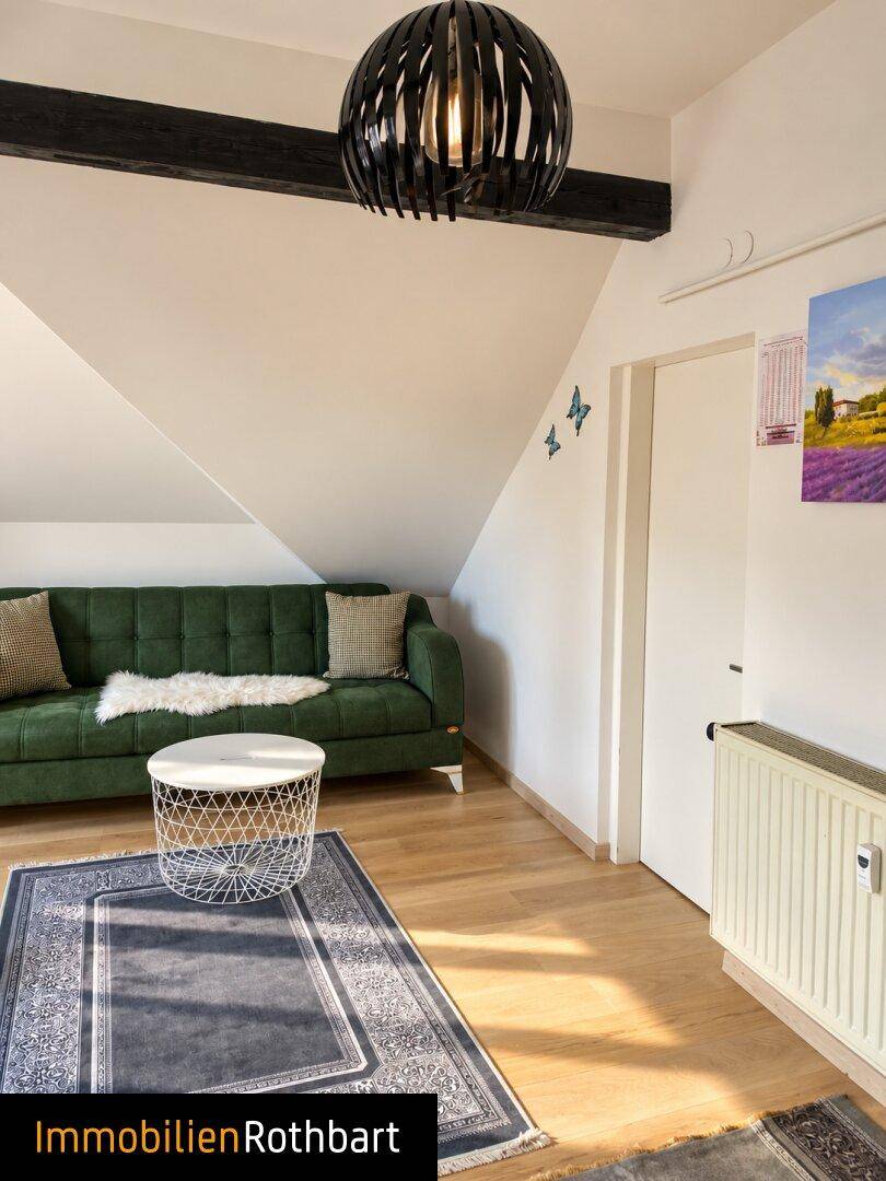Wohnbereich im Dachgeschoss mit grüner Couch, Holzboden und dekorativen Schmetterlingen an der Wand.