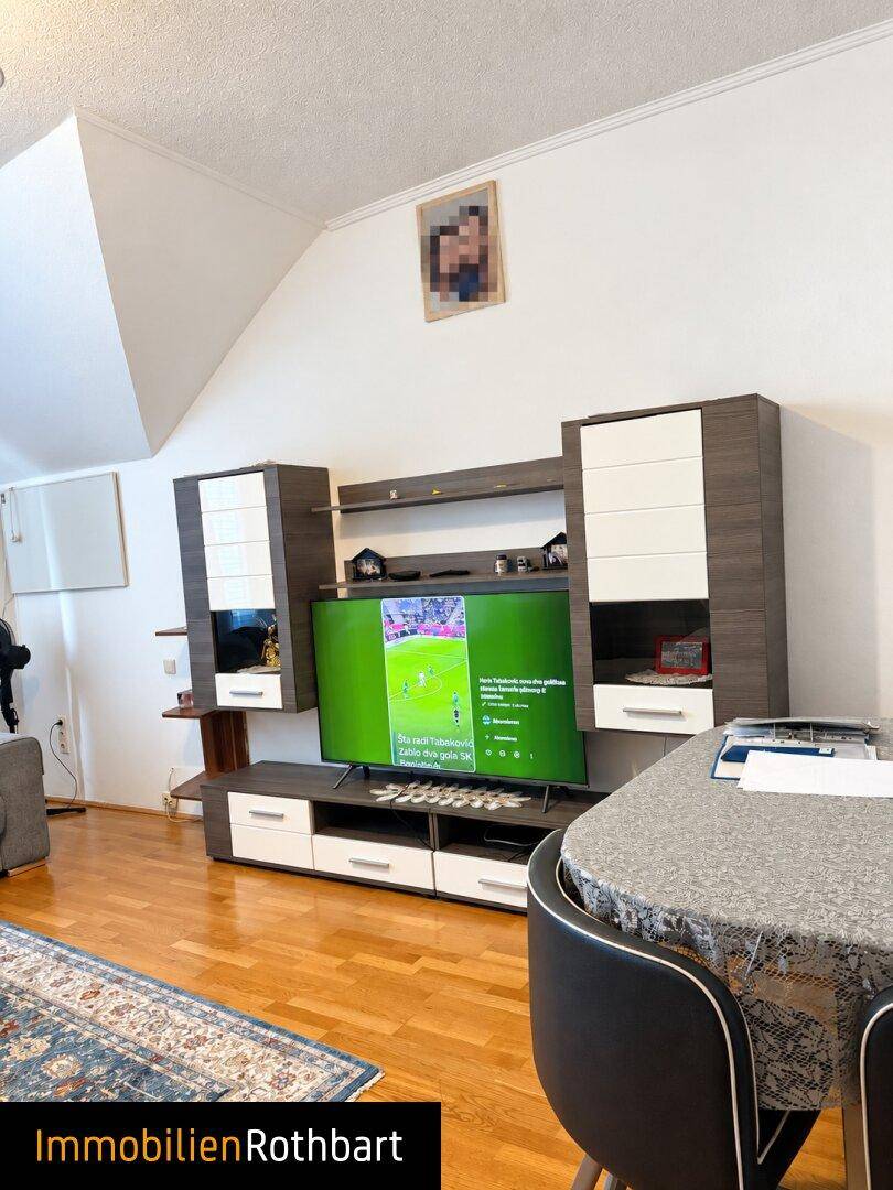 Wohnbereich mit Dachschräge, Holzboden und modernem TV-Möbel, ideal für Unterhaltung.