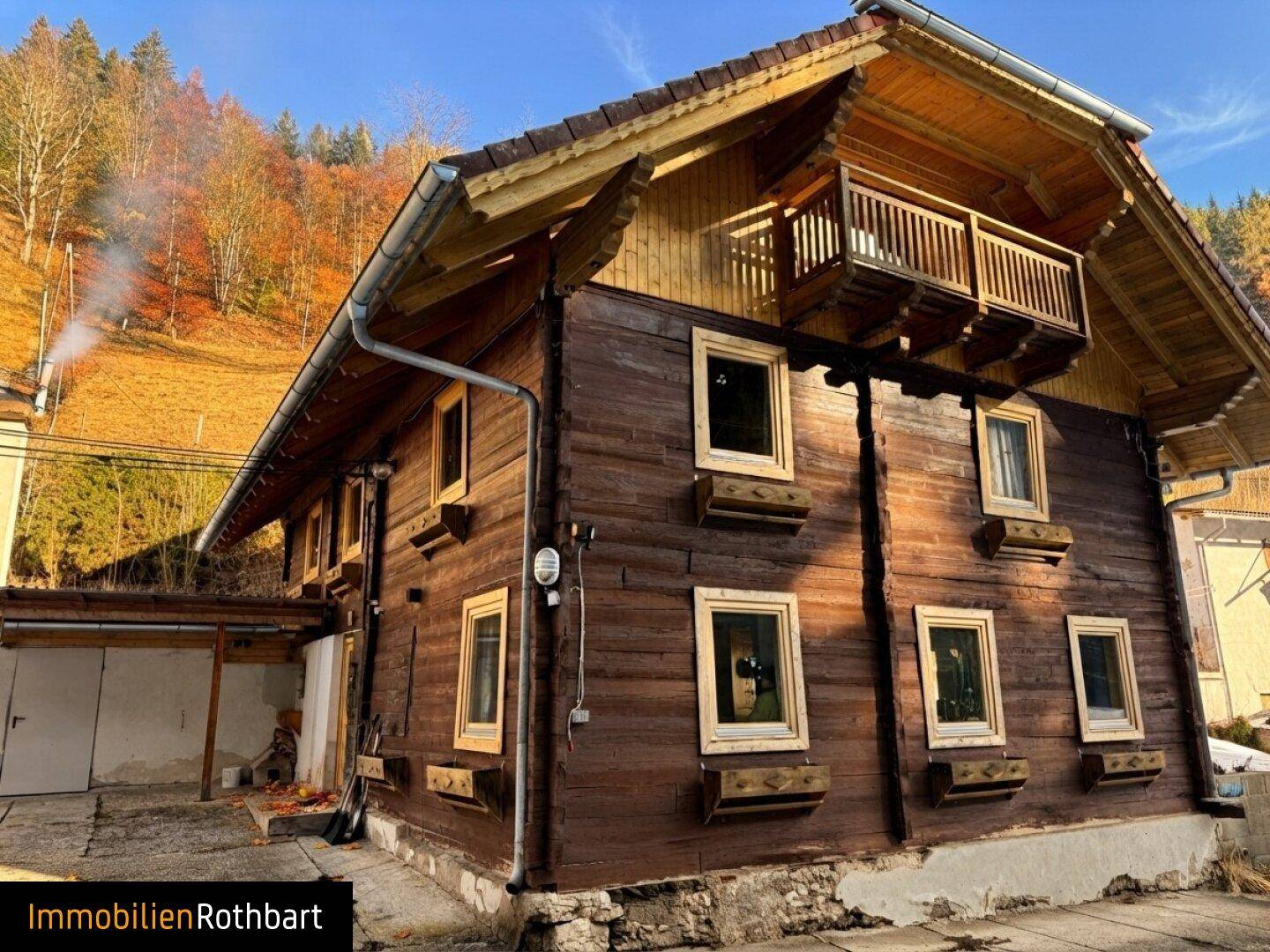 Seitenansicht des Holzhauses mit kleinem Balkon und Blick auf die bewaldeten Hügel.
