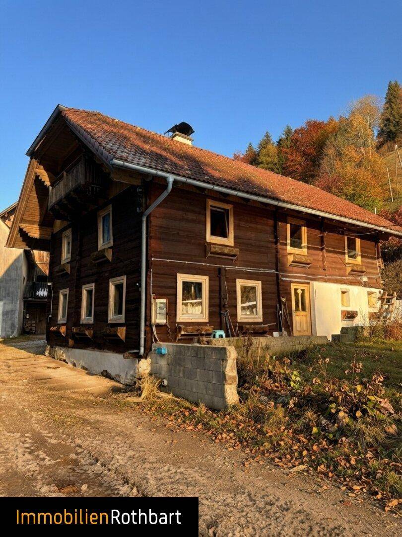 Traditionelles Holzhaus mit rotem Ziegeldach in ländlicher Umgebung und sonnigem Wetter.