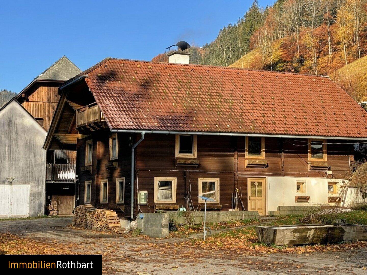 Traditionelles Holzhaus mit Holzstapel und rotem Ziegeldach in sonniger Lage.