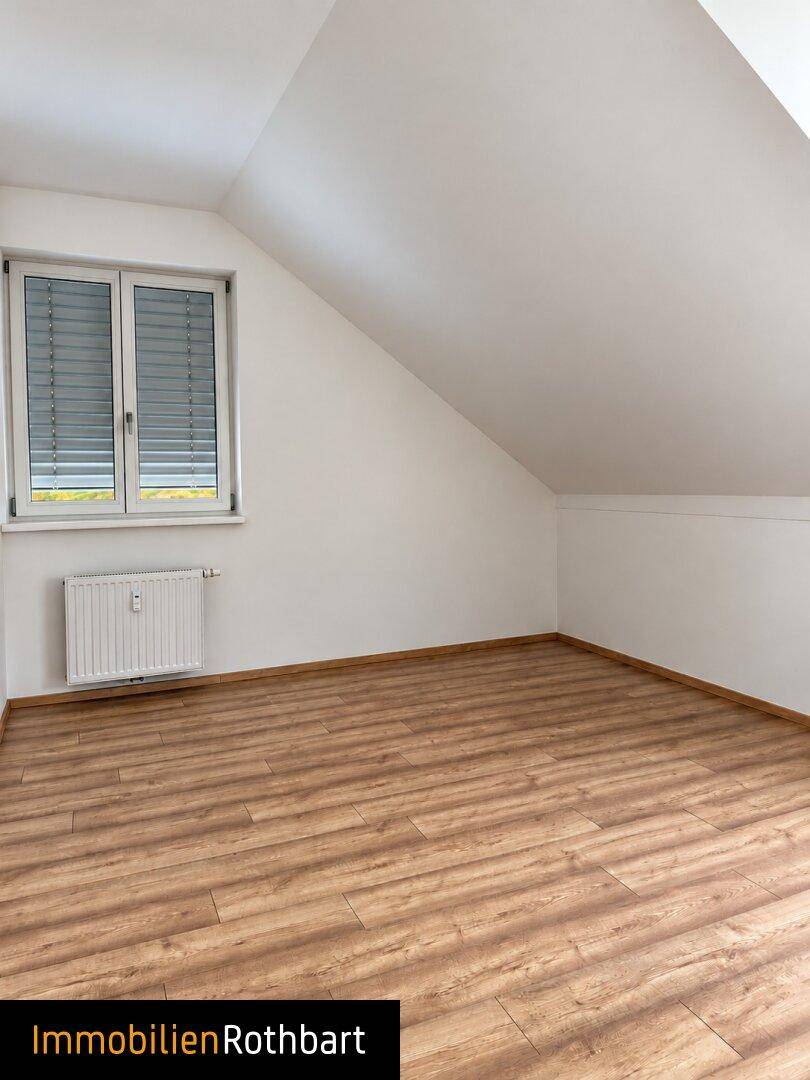 Heller Raum im Dachgeschoss mit Laminatboden, Heizkörper und Fenster mit Jalousien.