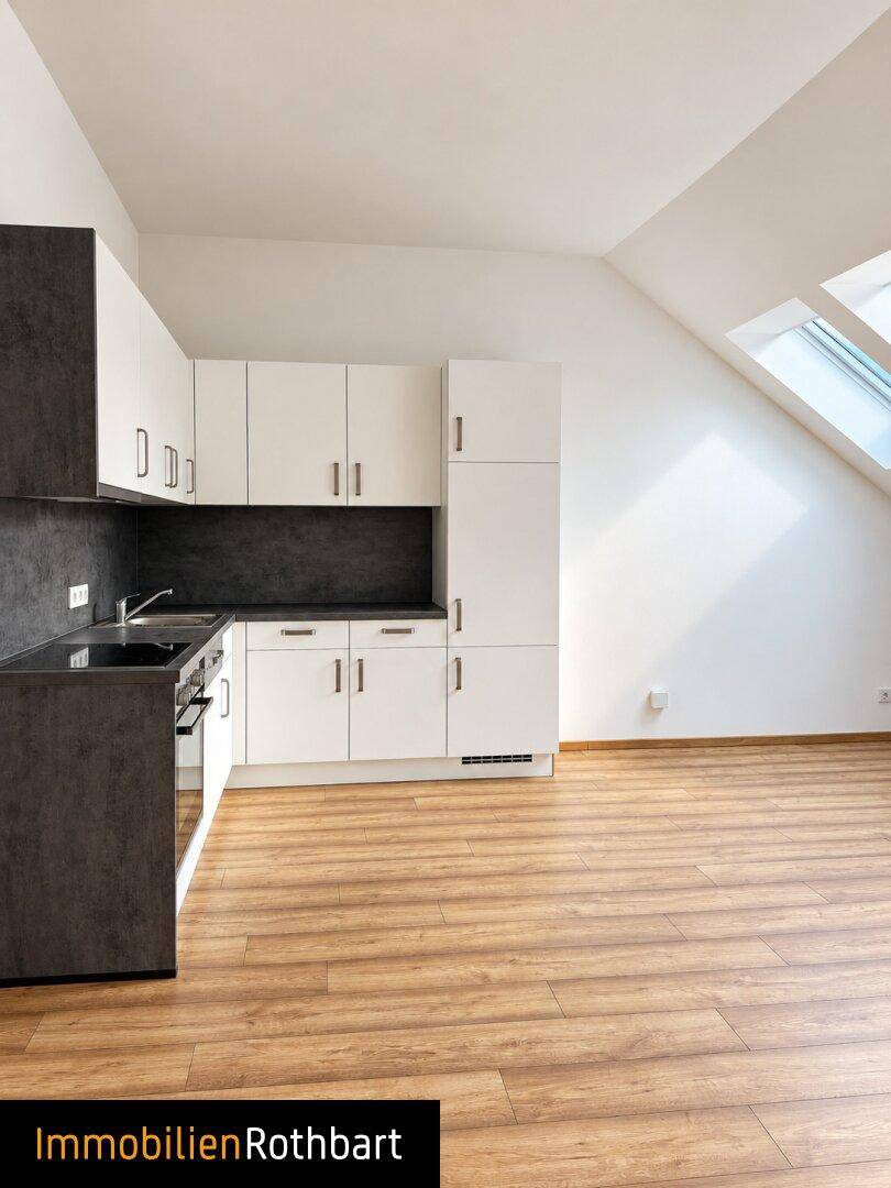 Helle Küche mit Dachschrägen und Dachfenstern, ausgestattet mit modernen weißen Schränken.